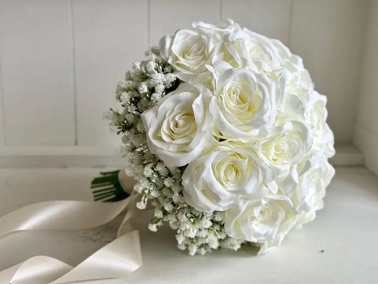 Bouquet de roses blanches orn&eacute; de gypsophile fleur, avec un ruban de satin cr&egrave;me.