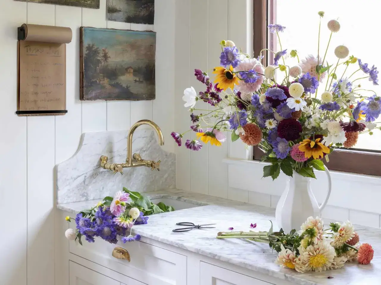 Un grand bouquet de fleurs sauvages dans un pichet blanc, prêt à être arrangé. Des fleurs coupées et des ciseaux sur le comptoir en marbre, pour savoir comment conserver un bouquet de fleurs.