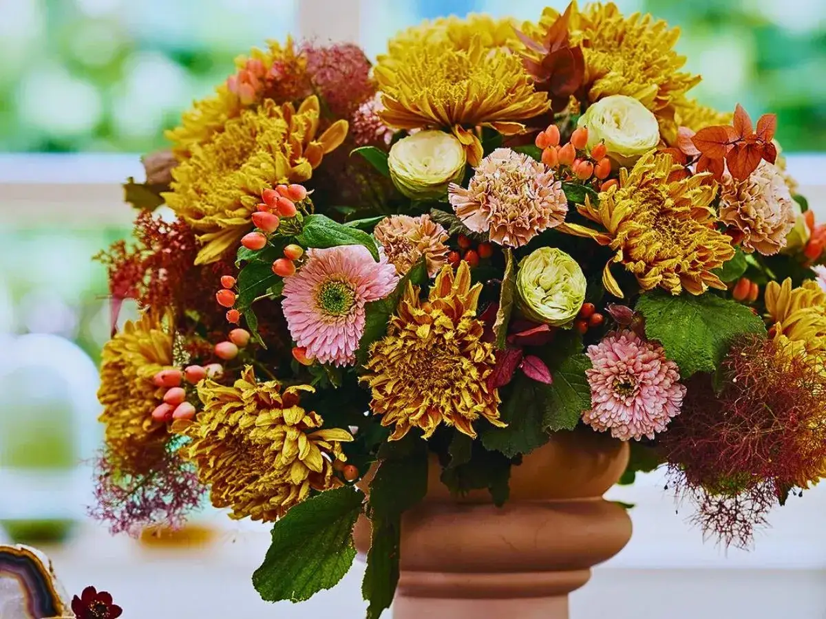 Magnifique composition automnale de chrysanth&egrave;mes jaunes, roses p&acirc;les, baies orang&eacute;es et feuillage dans un vase en terre cuite.