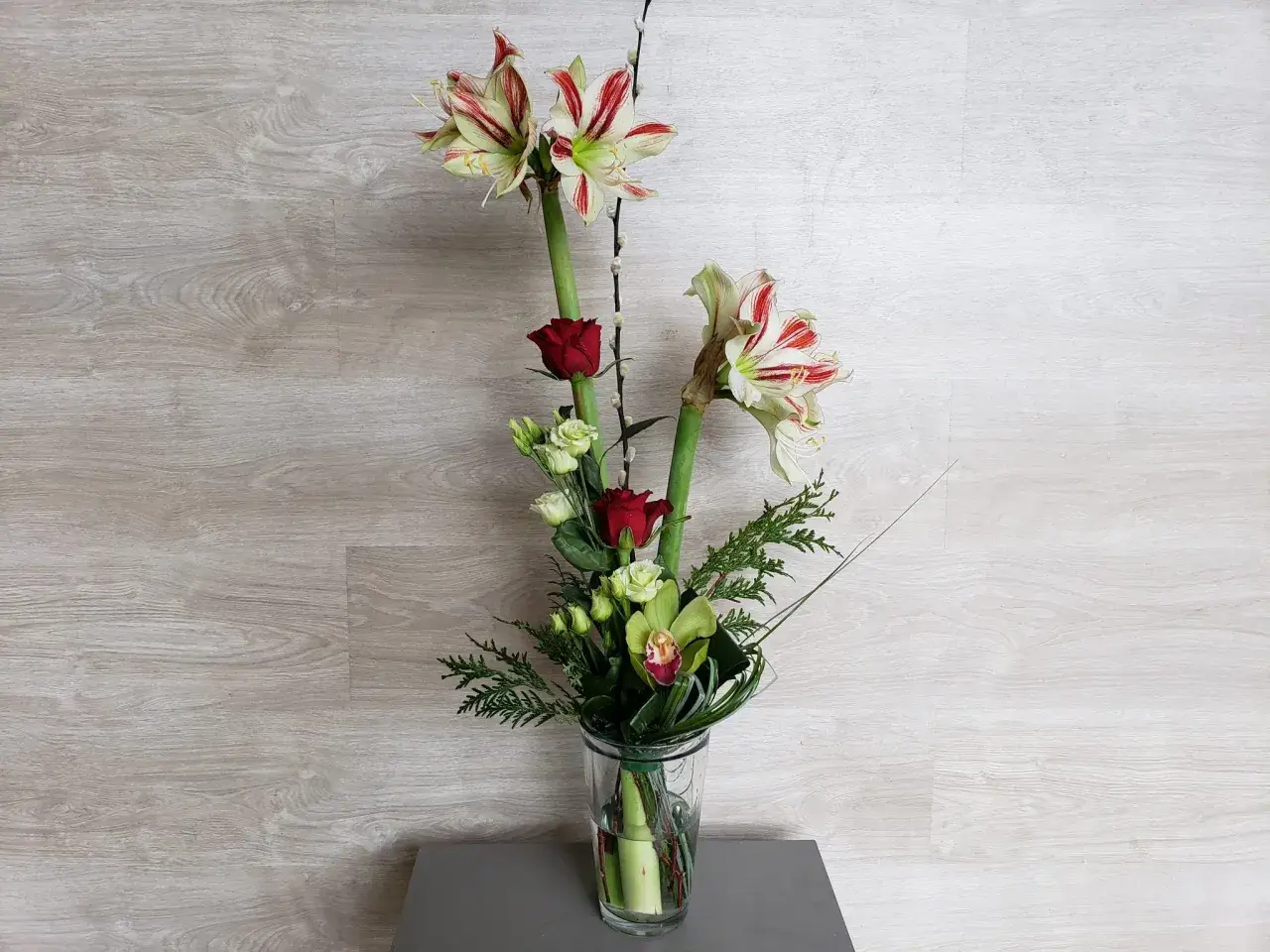Composition amaryllis avec roses rouges et orchidées vertes dans un vase en verre.